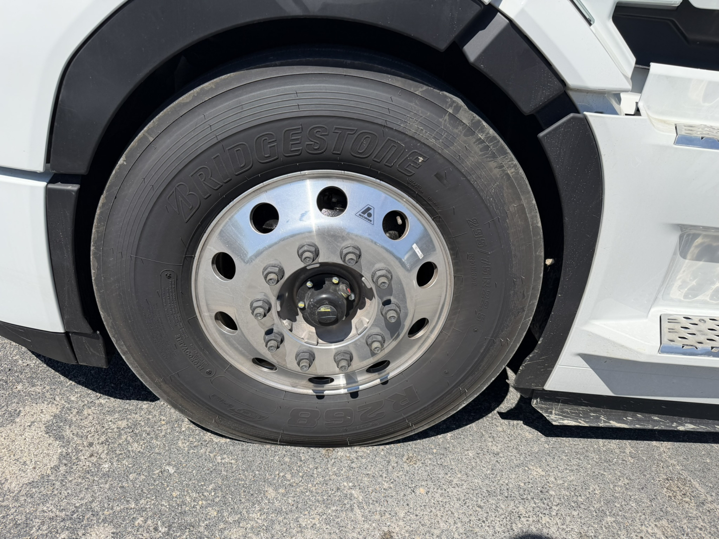 Bridgestone tire on Mack truck wheel with silver rim and lug nuts; partial view of front fender and bumper.