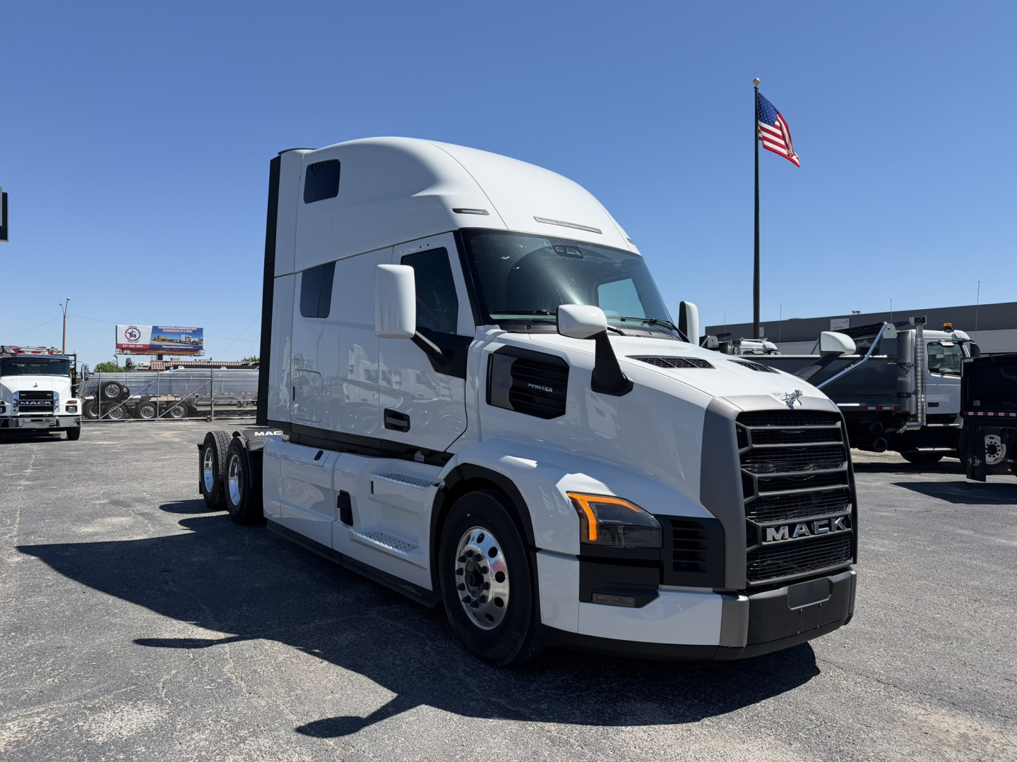 2017 Mack PR64T76H tractor-trailer truck in a dealership lot, white cab, chrome grille with MACK emblem, black bumper, American flag in background, multiple trucks