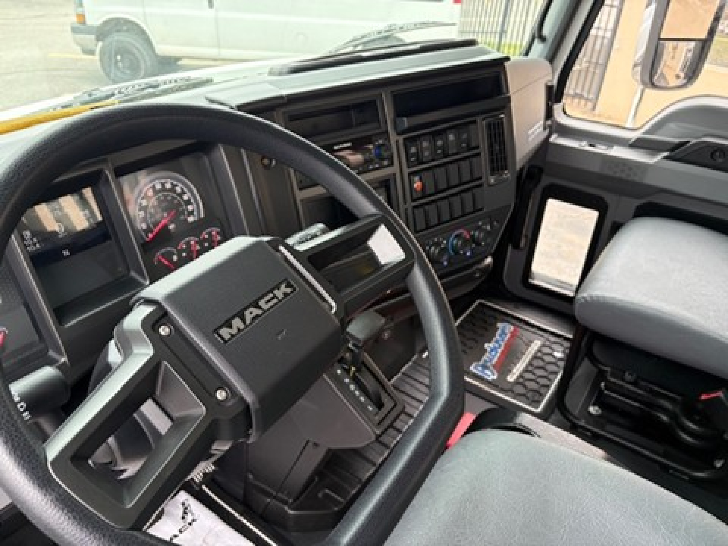 Mack MD6 driver’s cockpit showing steering wheel with Mack logo, dashboard gauges, and control panel with radio and climate controls.