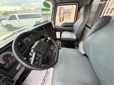 Vehicle cabin of a 2025 Mack MD6, driver seat and steering wheel in view, dashboard gauges, center console, and entry door visible.