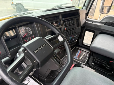Mack MD6 driver’s cockpit showing steering wheel with Mack logo, dashboard gauges, and control panel with radio and climate controls.