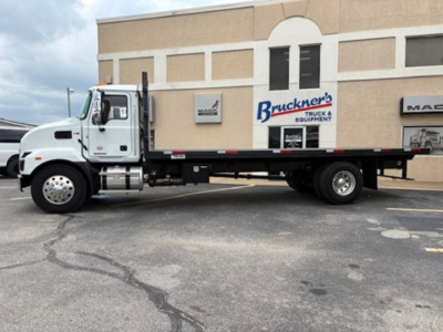 Flatbed truck in front of a building with Bruckner’s Truck & Equipment sign; Mack MD6 cab visible, white color, long flatbed.