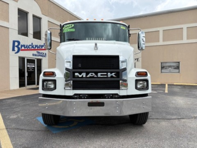 Mack MD6 front view showing bold grille with MACk lettering, large bumper, and side mirrors; flatbed truck in dealership lot.