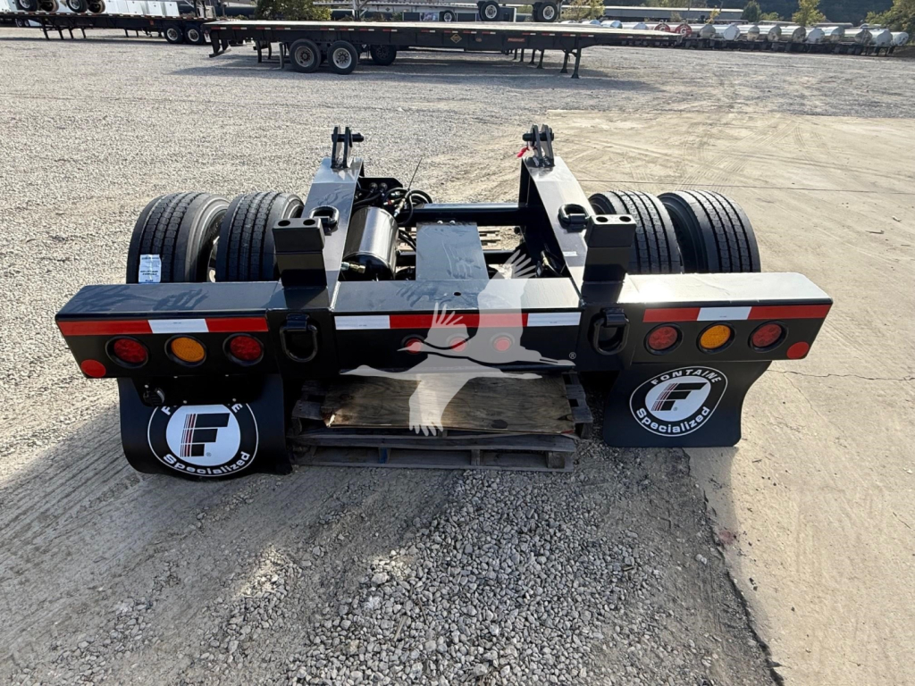 Fontaine flip axle trailer rear view with dual axles, wiring, and taillights in a storage yard.