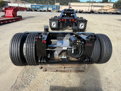 Fontaine flip axle trailer component showing dual axles with heavy-duty suspension and hydraulic lines, mounted on a pallet in an outdoor lot.