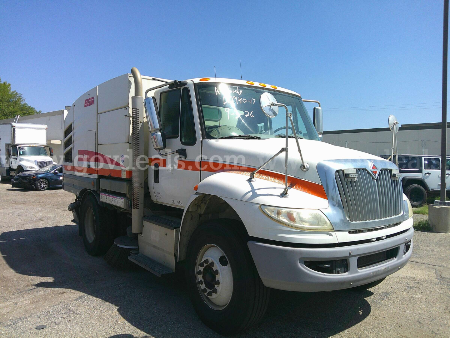 International DuraStar 4400 street sweeper truck in white with orange stripe, front grille, dual mirrors, side access steps, and swept debris body.