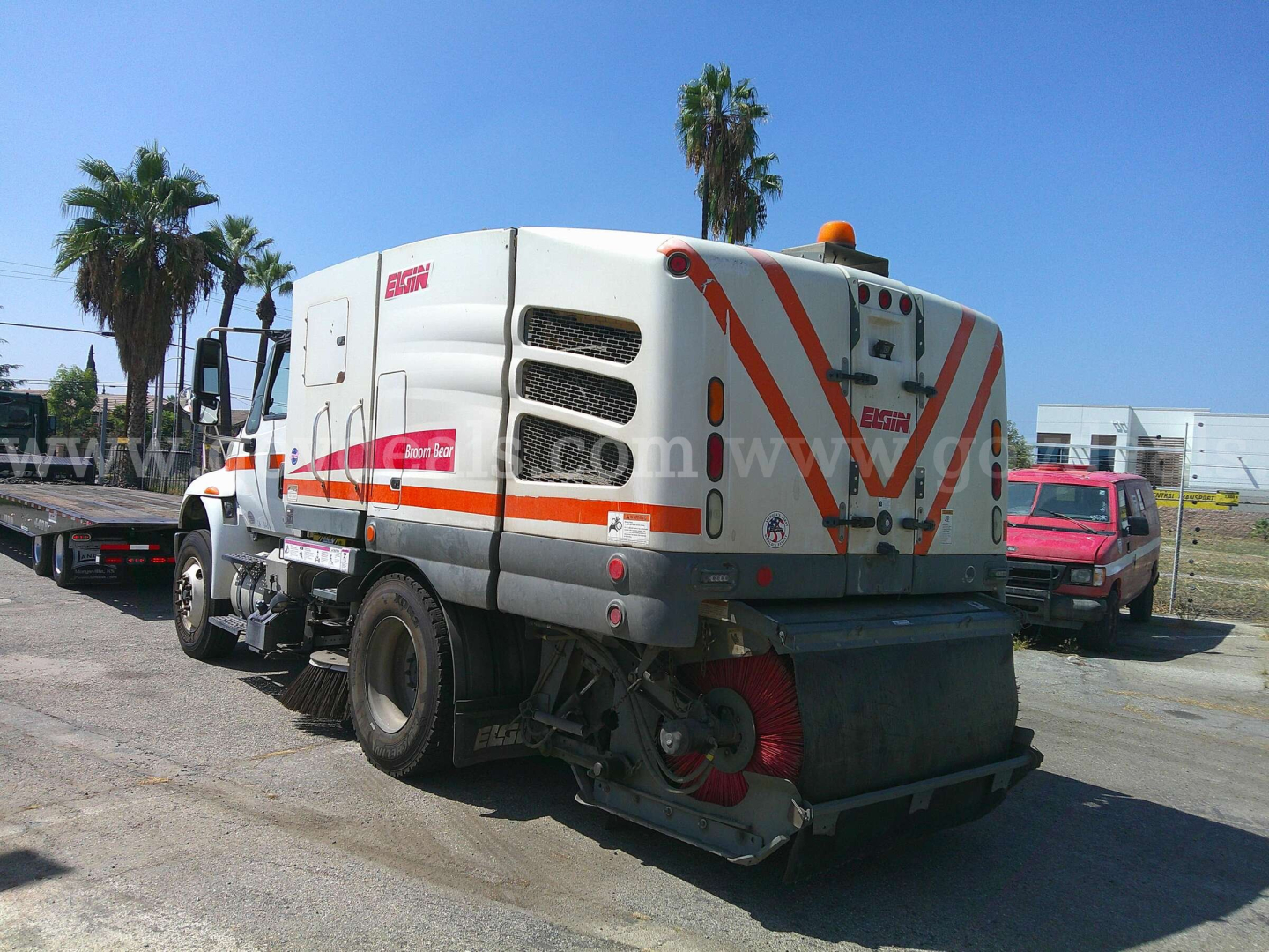 Truck rear view of a street sweeper: International DuraStar 4400 with orange safety stripes, compact rear suction housing, and side decals.