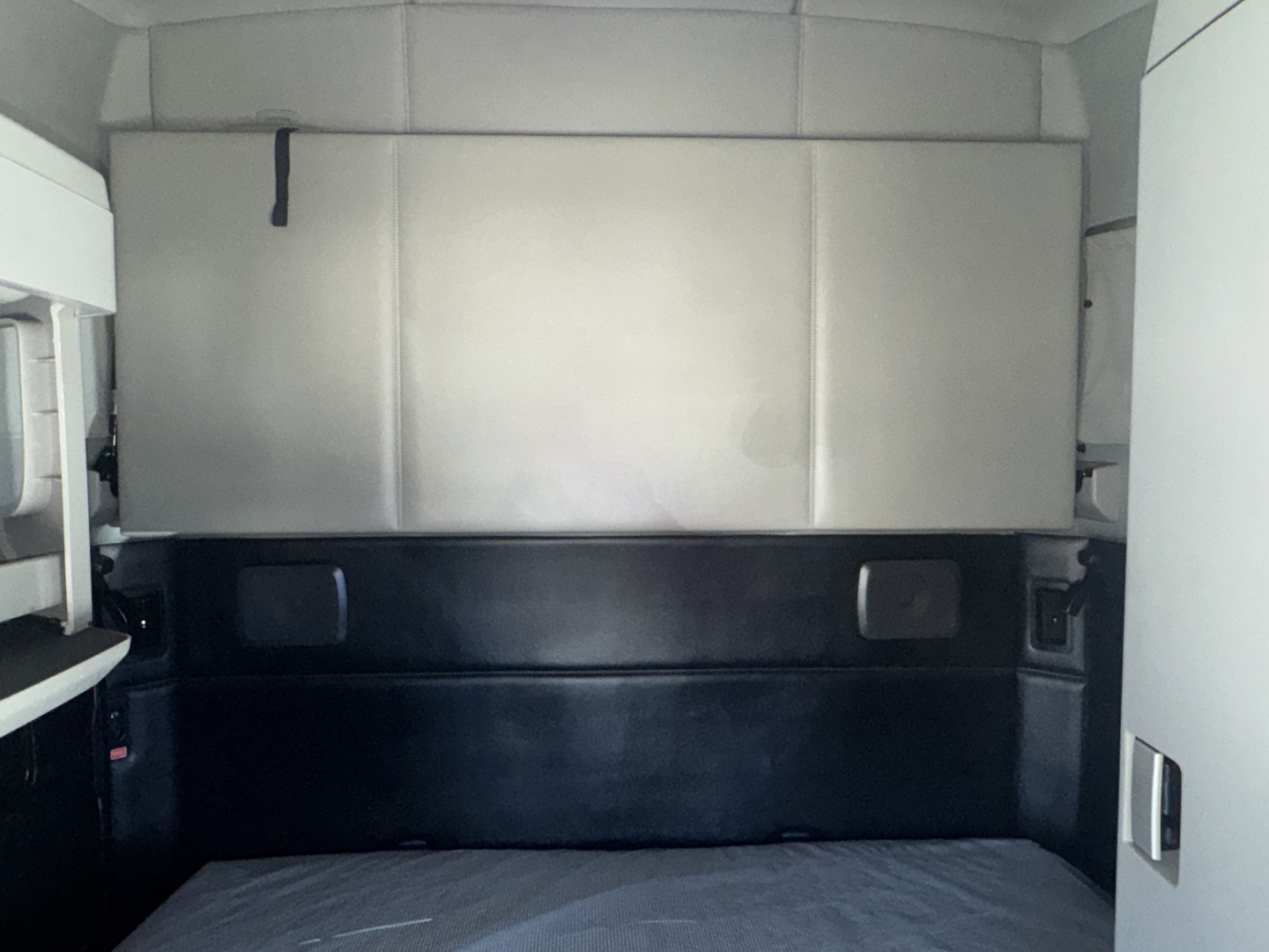 Truck cab interior showing a sleeping area with metallic walls and black lower panel, no visible text, vinyl mattress flat surface.