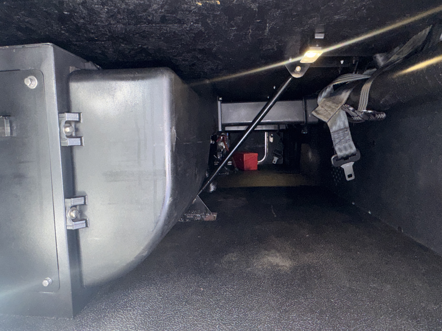 Kenworth T680 cab interior under dash showing wiring, floor, and a rectangular component/box with mounting brackets.
