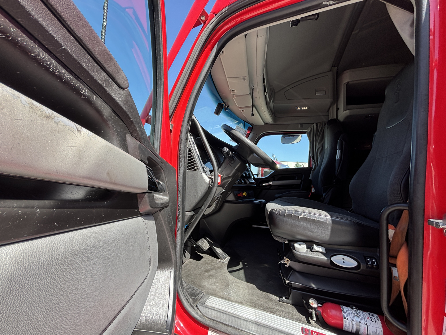 Kenworth T680 cab interior showing driver seat, steering wheel, and dashboard with door open.