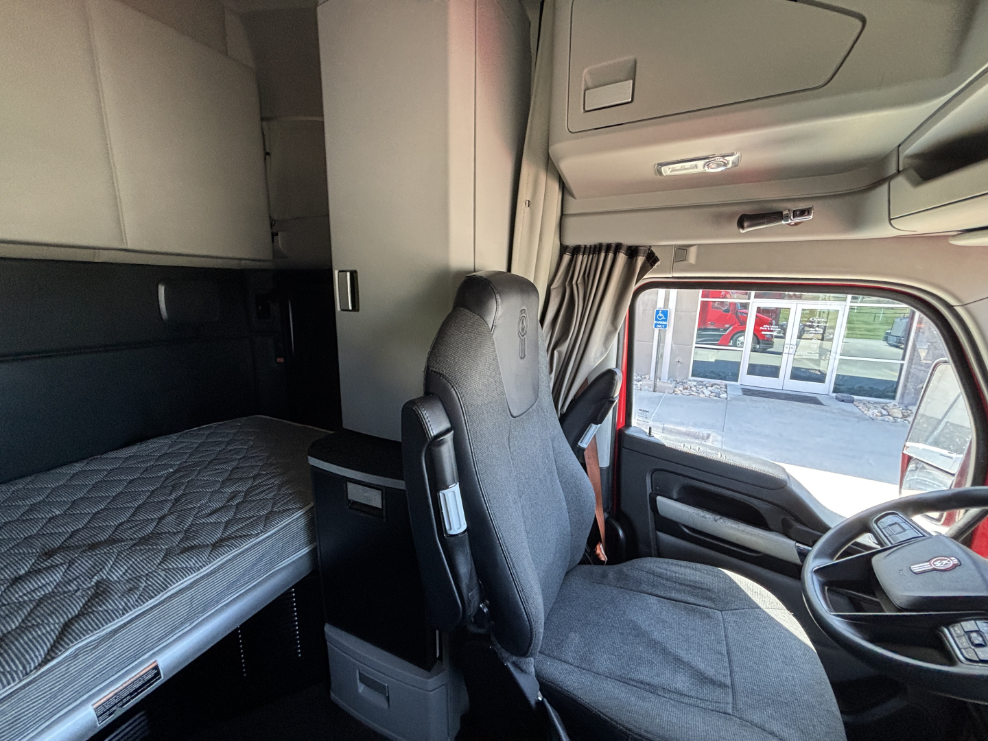 Kenworth T680 interior cabin and sleeper area showing driver's seat, dashboard, and a bed in the sleeper compartment.