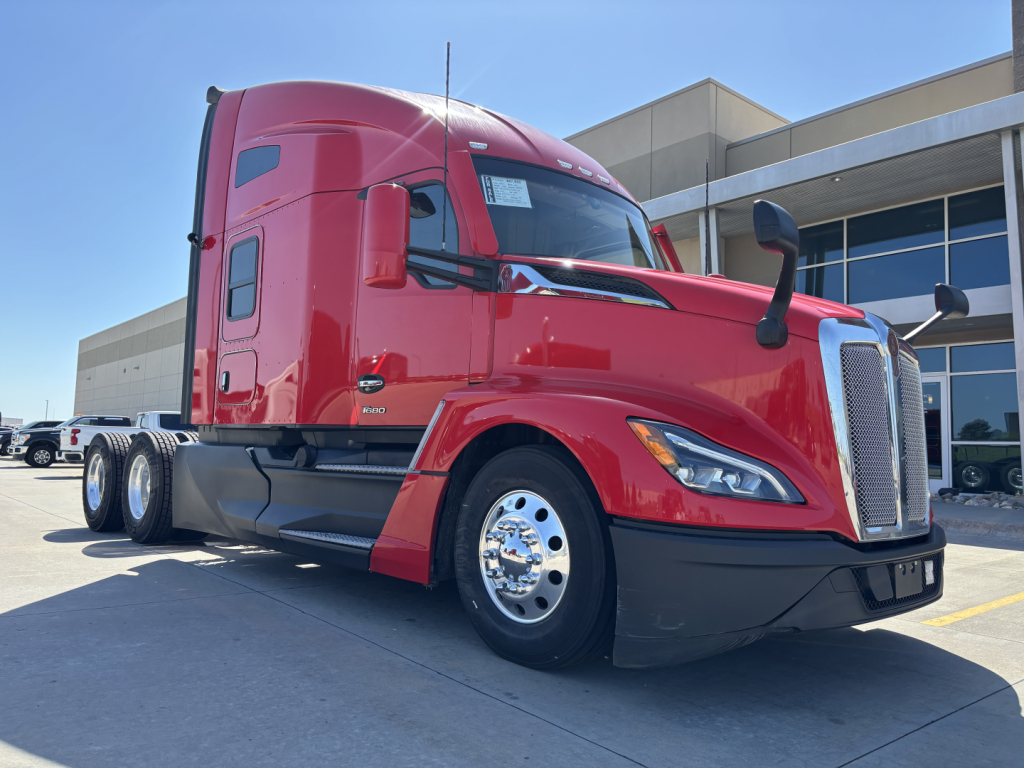 Kenworth T680 conventional sleeper tractor in red, front-left view showing cab, doors, mirrors, chrome wheels, and aerodynamic fairings.