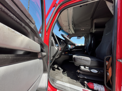 Kenworth T680 cab interior showing driver seat, steering wheel, and dashboard with door open.
