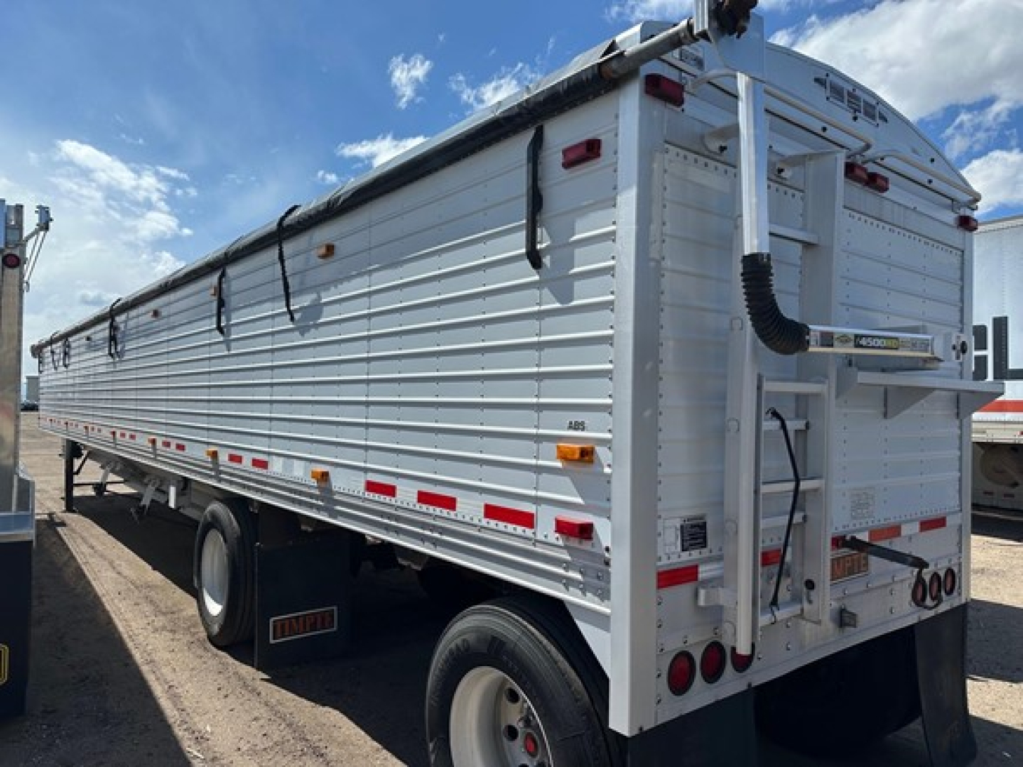 Timpte Super Hopper trailer viewed from side and rear showing aluminum body, rear hopper doors, stacked chains, and taillights.