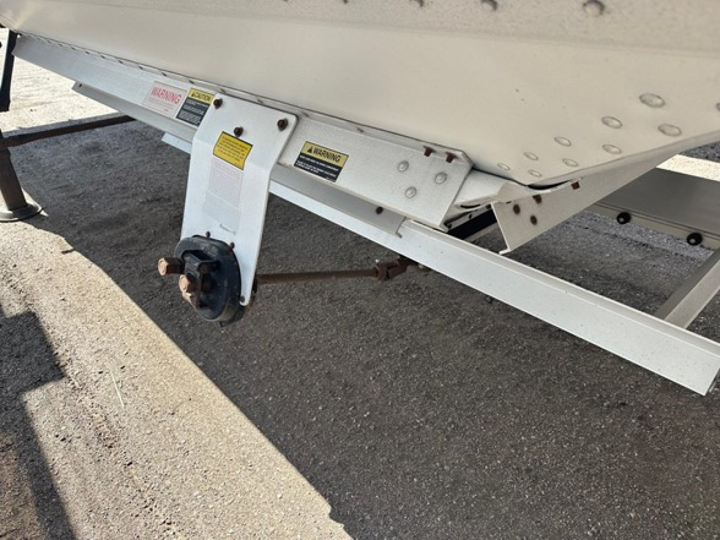 Trailer undercarriage showing a Timpte hopper trailer with a landing gear wheel hub and warning labels on a white steel frame.