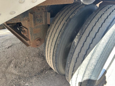 Trailer rear axle assembly and dual tires with rusty frame component visible.