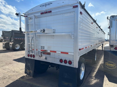 Rear of a white Timpte hopper trailer with multiple red tail lights, bumper, and license plate area. Visible small label and hinges on the tailgate, and mudflaps behind wheels.