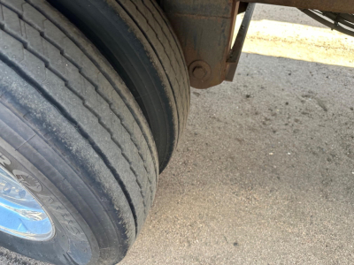 Tandem axle trailer wheel area showing dual tires with chrome hubcap and part of the undercarriage.