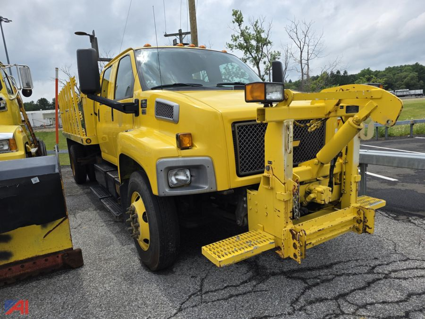 Front view of a yellow 2008 Chevrolet Kodiak C7500 stake truck with a mounted front snow/plow or lifting attachment, dual rear wheels, and black grille.