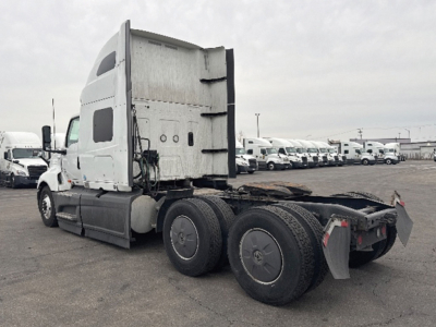 Truck tractor in a yard showing rear of cab and triple axles with fifth-wheel; International LT625 model with white cab and gray chassis.