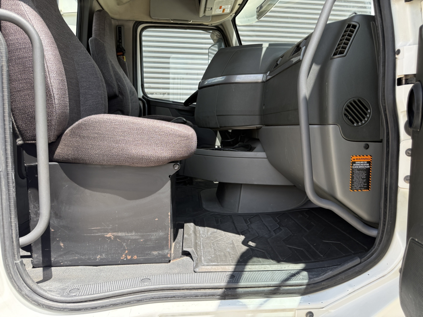 Volvo VNL300 cab interior with driver seat and dashboard view from open door, showing steering area and floor mat.
