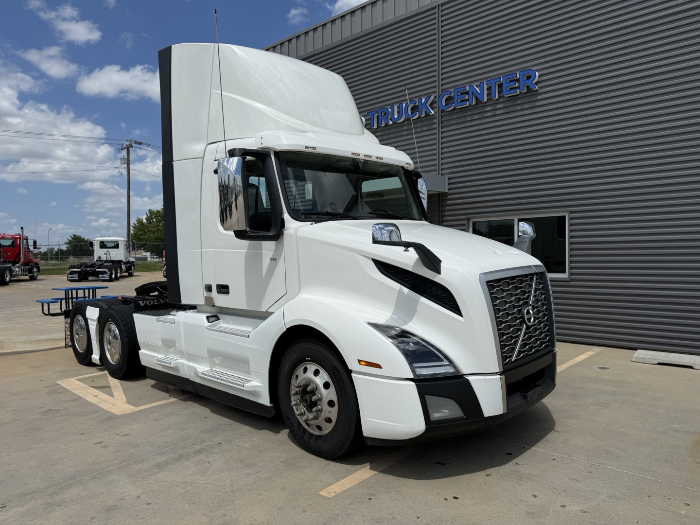 Volvo 2019 VNL300 conventional daycab tractor in white parked outside a truck center showing cab with aerodynamic mirrors and sleeper area.
