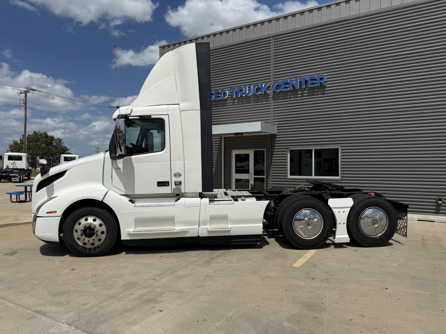 Volvo VNL300 daycab tractor in front of dealership showing sleeper cab, side view, white exterior, three rear axles, stock number B3451P.