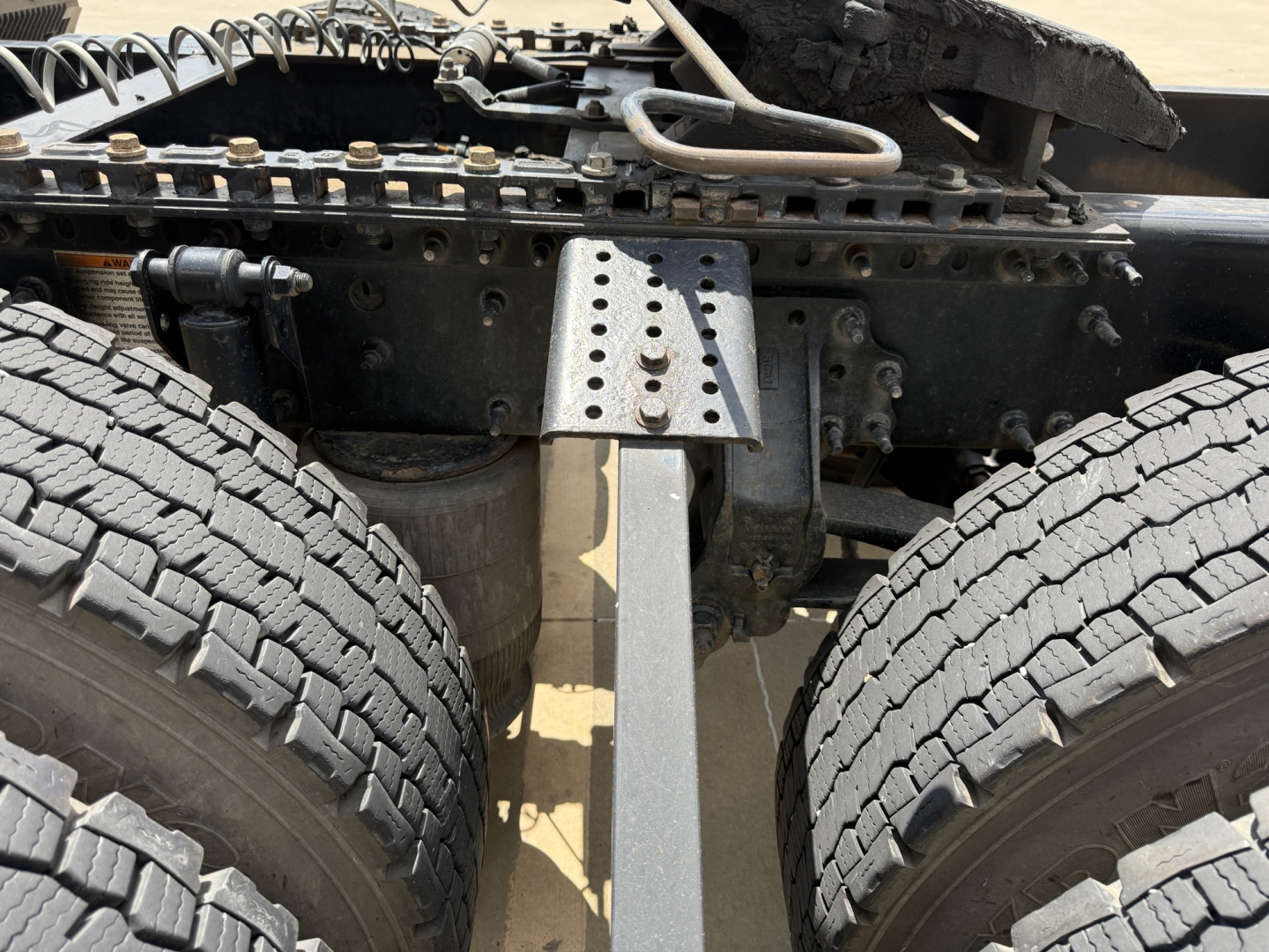 Truck rear undercarriage showing dual rear axles and frame with perforated metal brace and suspension components.