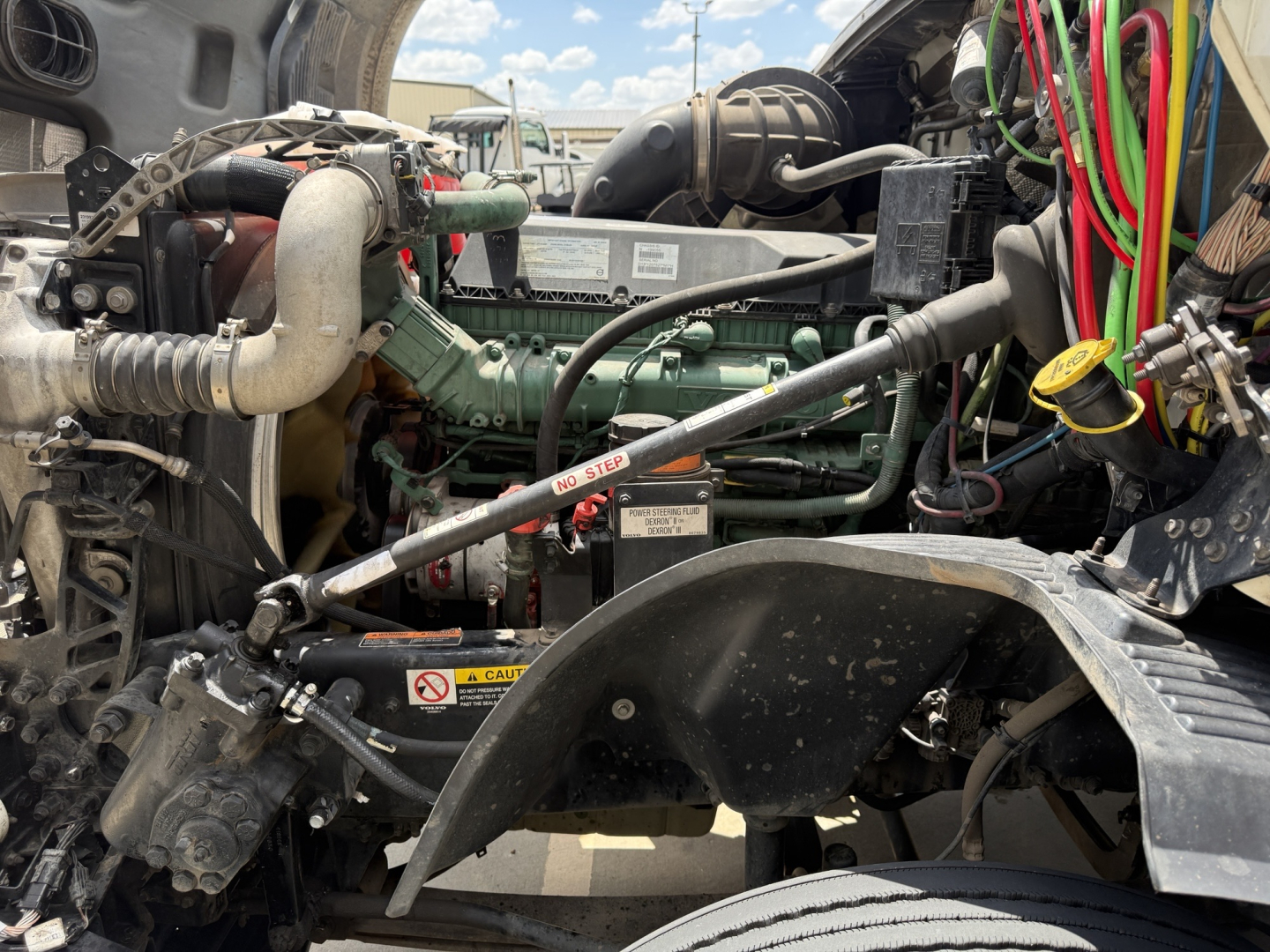 Engine bay of a 2019 Volvo VNL300 daycab showing green Volvo engine, hoses, wiring, and nearby components in view.
