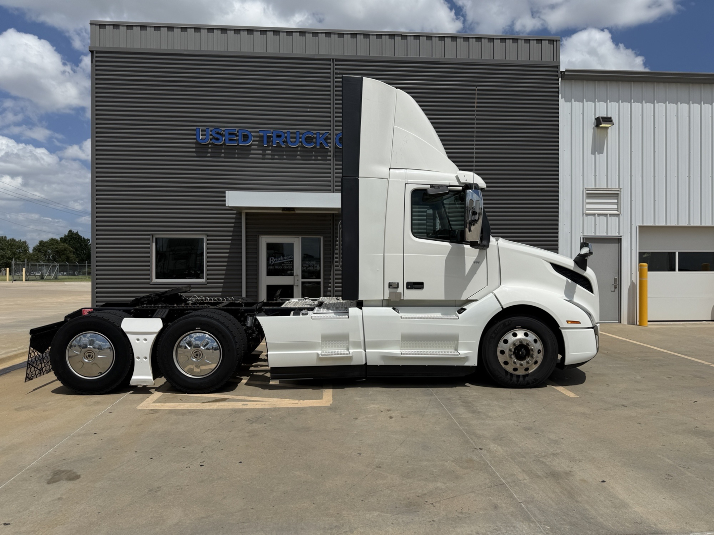 Volvo VNL300 sleeper cab tractor in side profile view, white exterior, with two rear axles, parked in lot in front of used truck center.