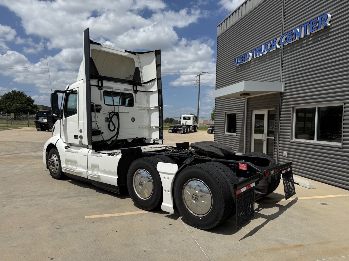 Volvo VNL300 truck tractor rear and side view showing sleeper cab, white exterior, dual rear axles, with hitch area and dealership building in background.