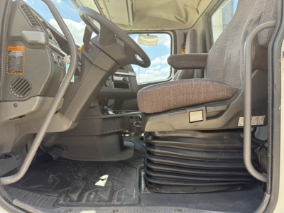 Cab interior of a Volvo VNL300 truck showing steering wheel, driver's seat, and floor mat with a beige seat cushion and ribbed base.