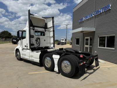 Volvo VNL300 truck tractor rear and side view showing sleeper cab, white exterior, dual rear axles, with hitch area and dealership building in background.