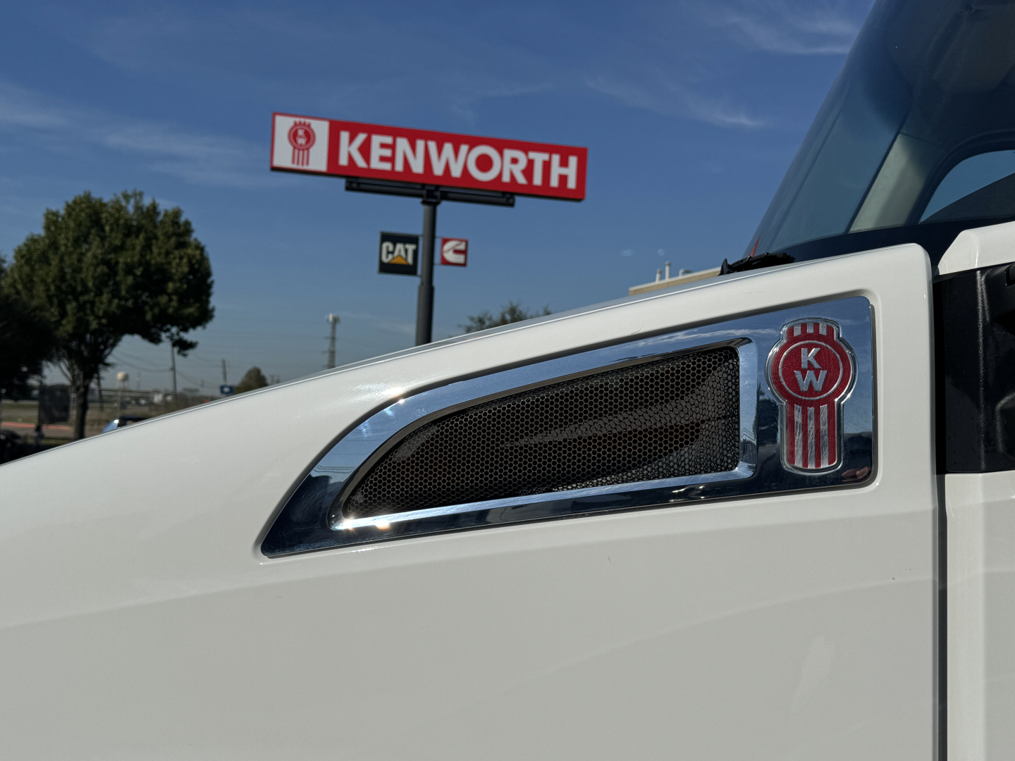 Kenworth T680 truck cab side with emblem and air intake, Kenworth sign in background.