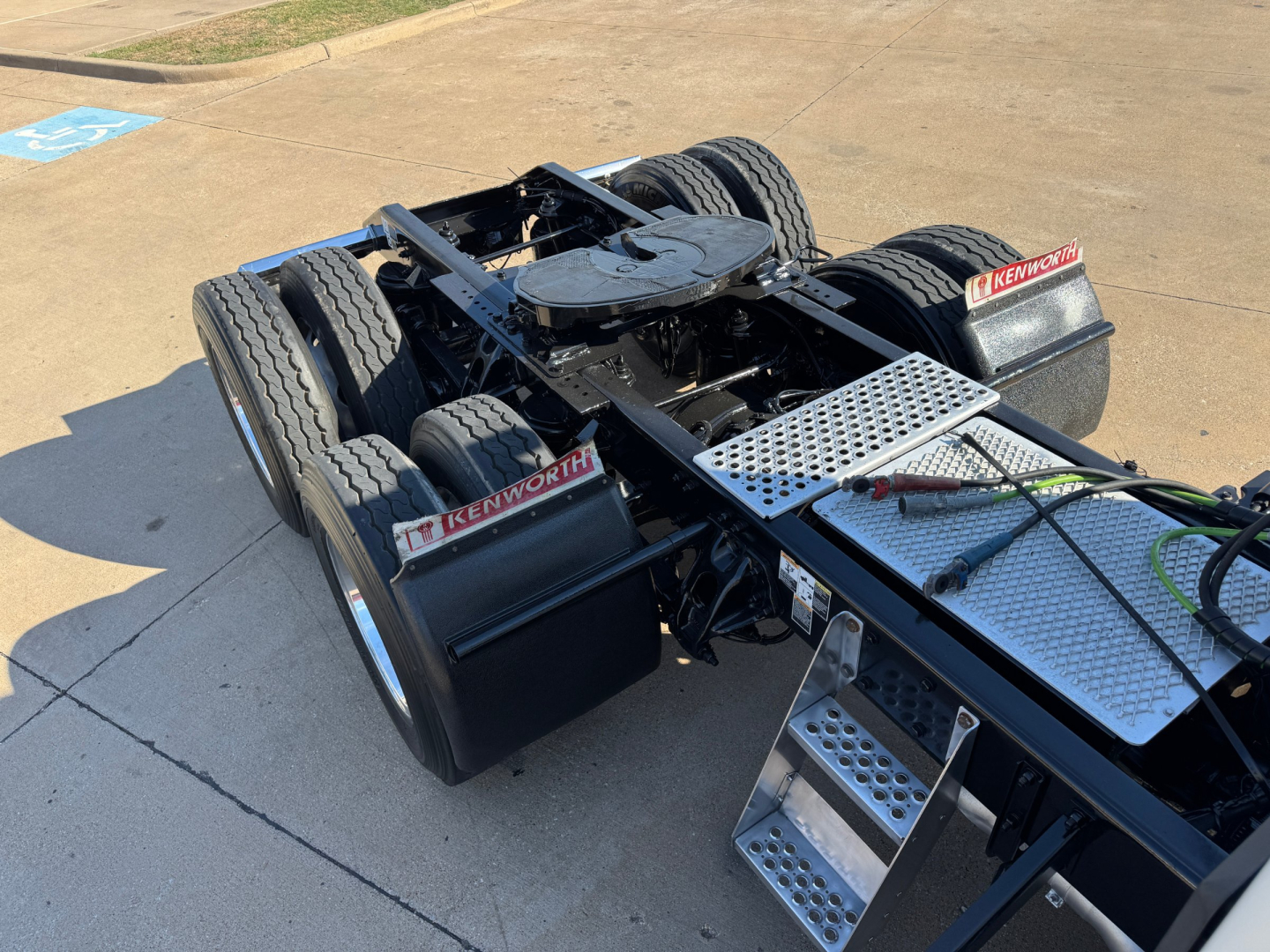 Kenworth T680 tractor chassis showing dual rear axles and metal diamond-plate steps with Kenworth branding on the mud flaps.