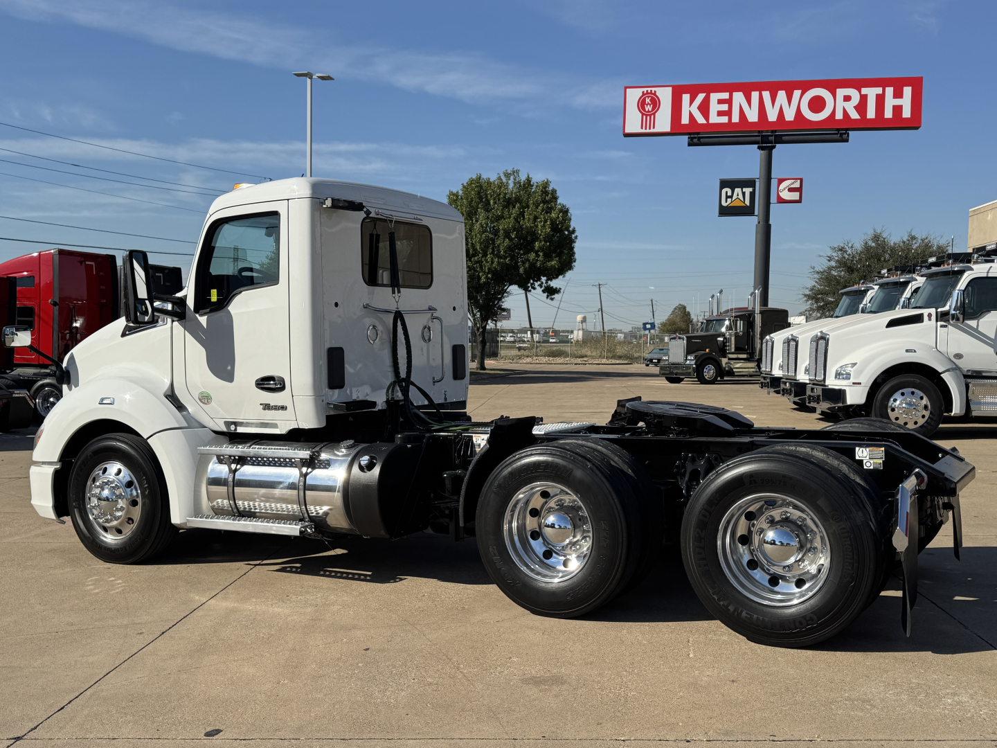 Kenworth T680 tractor in white, side view showing cab, fuel tanks, and dual rear axles at a dealership lot.