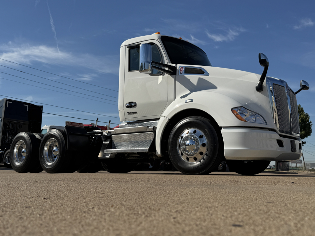 Kenworth T680 conventional daycab truck side/front view showing white cab, chrome grille, dual rear axles, and chrome wheels.