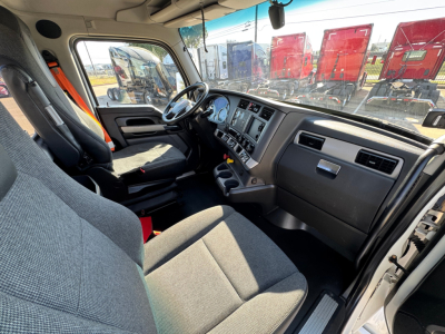Kenworth T680 truck cabin interior with steering wheel, dashboard, and gray fabric seats. Visible pickup from driver seat showing instrument cluster and central console.