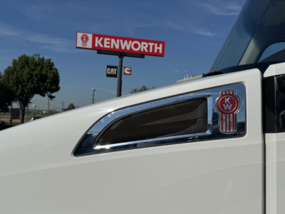 Kenworth T680 truck cab side with emblem and air intake, Kenworth sign in background.