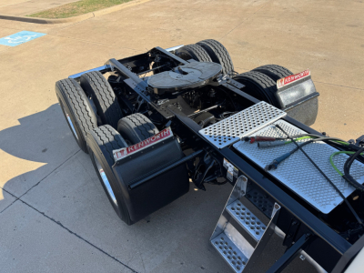 Kenworth T680 tractor chassis showing dual rear axles and metal diamond-plate steps with Kenworth branding on the mud flaps.