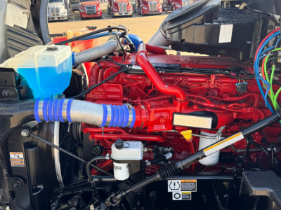 Kenworth T680 engine bay showing red engine block, blue coolant reservoir, silver hoses with blue clamps, white oil filter, and various black wiring harnesses.