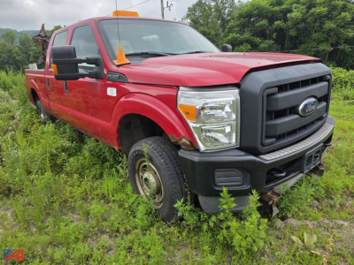 Ford F-350 Super Duty pickup truck with plow mount, red cab, crew cab, black front grille, standing in tall grass.