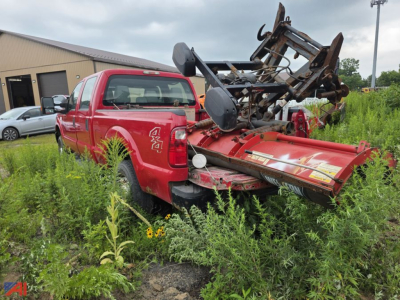 Ford F-350 Super Duty crew cab pickup with attached plow in overgrown lot; blade and mounting hardware visible.