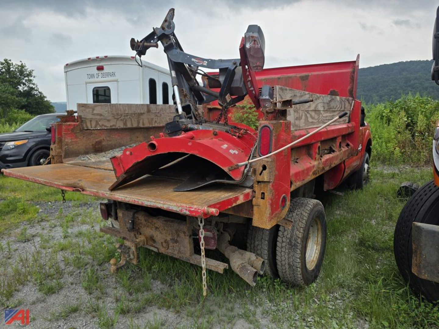 Dump truck bed with plow attachment and hydraulic arms on a 2016 Ford F-350 Super Duty dump truck, red with wooden side rails, muddy chassis.