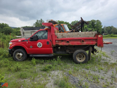 Ford F-350 Super Duty dump truck with plow showing red cab and dump bed, field setting, some equipment in bed.