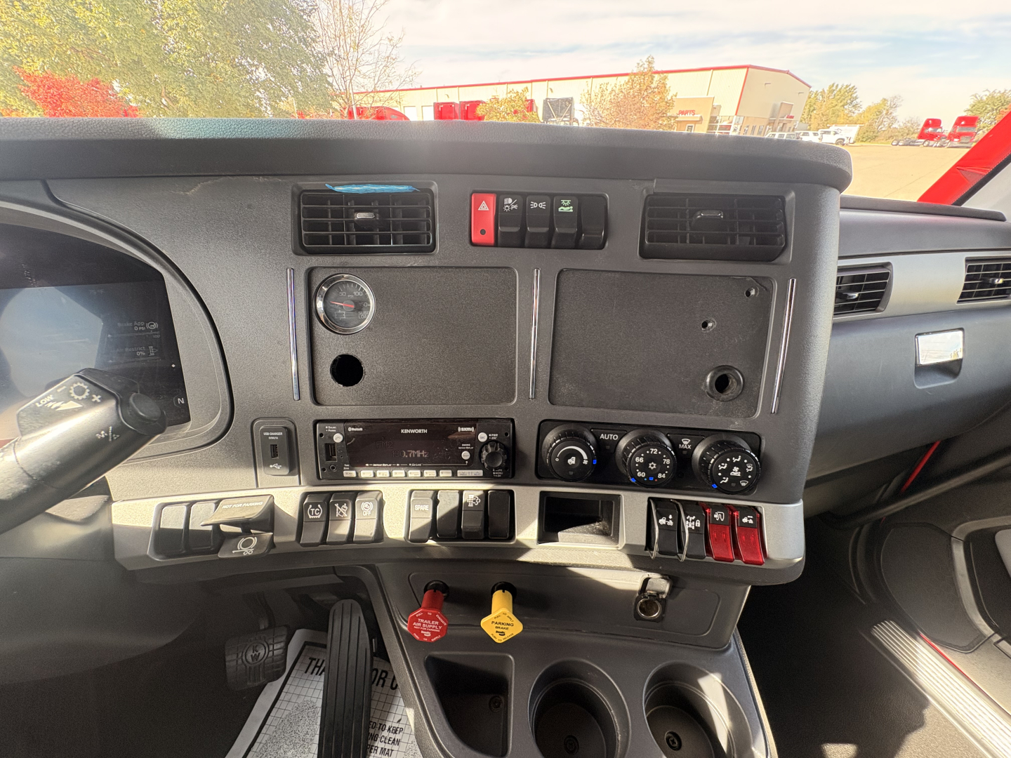 Cab interior of a 2023 Kenworth T680 dash showing controls, vents, gauges, and dash panels with red and yellow toggle keys.