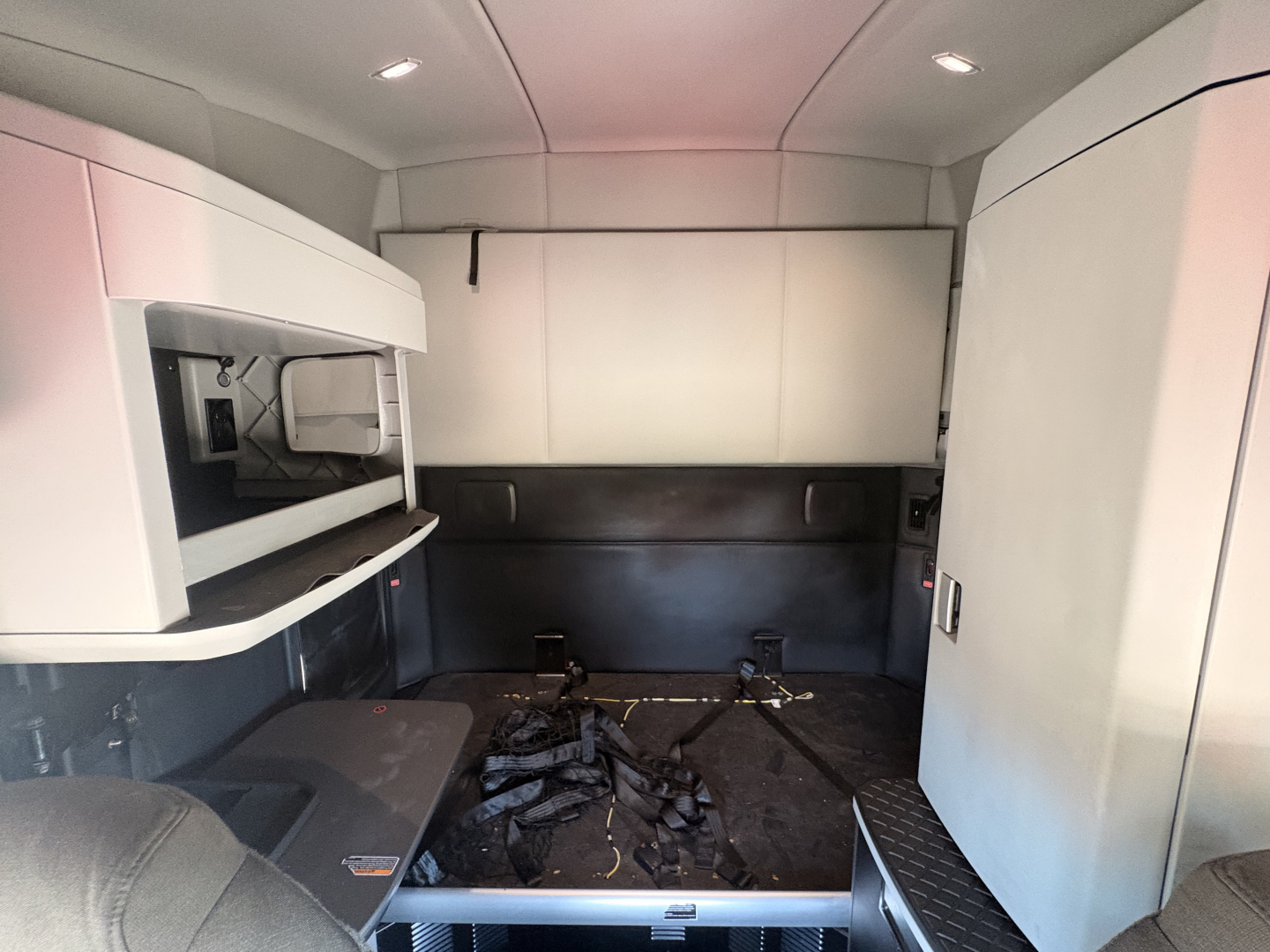 Kenworth T680 sleeper cab interior showing bunk area and storage cabinets with seat belts on the floor.