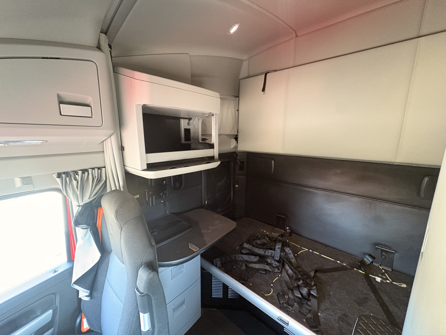 Kenworth T680 truck sleeper cab interior view showing seating and storage area with overhead bunk and desk.