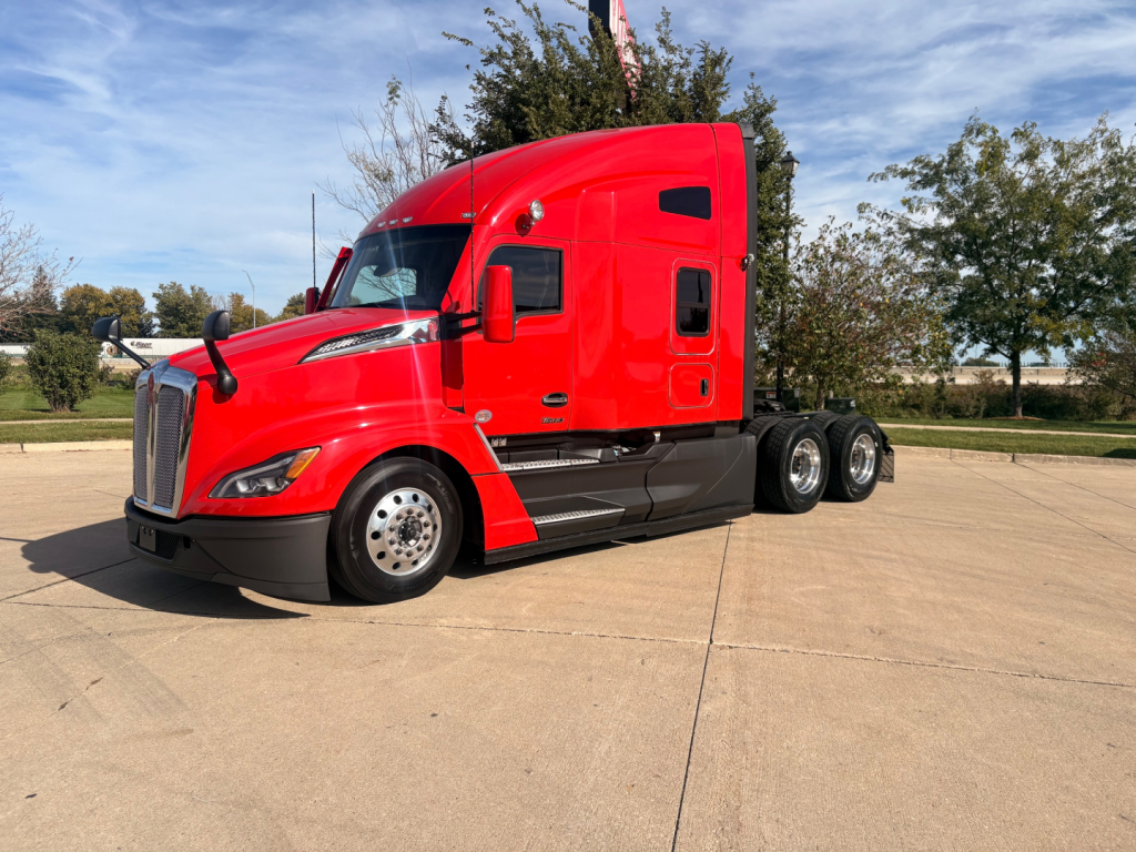 Kenworth T680 tractor-trailer in red, front-left view showing cab, wheel, and sleeper area.