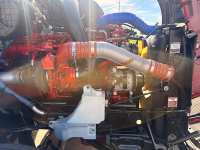 Kenworth T680 engine bay showing red engine components, large silver intake, blue silicone hoses, coolant reservoir, and black radiator support.